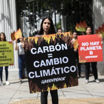 Activistas de Greenpeace sostienen carteles contra el uso de carbón y a favor de la acción climática frente a un edificio gubernamental.