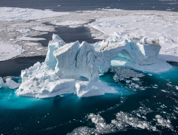 El deshielo polar rompe récords: el hielo marino alcanza su mínimo histórico en febrero de 2025 Vista aérea de un iceberg desgajado flotando en aguas oscuras, rodeado de fragmentos de hielo marino, evidenciando el derretimiento acelerado en los polos.