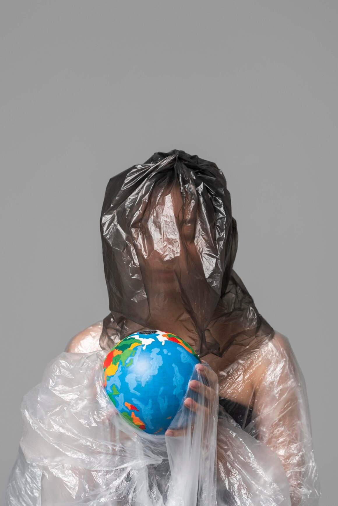Mujer envuelta en plástico sosteniendo un globo terráqueo como símbolo de la contaminación por plásticos y la necesidad de alternativas sostenibles.