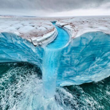 Cascada de deshielo glaciar cayendo al océano desde un bloque de hielo azul, símbolo del retroceso de los glaciares por el calentamiento global.