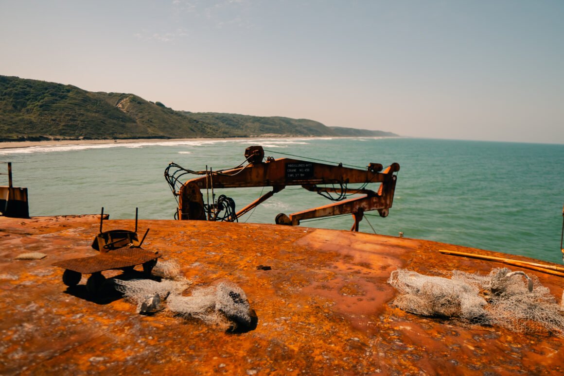 Vista de un barco oxidado con grúa marina abandonada frente a la costa, representando el impacto humano en el océano.