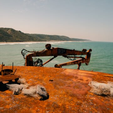 Vista de un barco oxidado con grúa marina abandonada frente a la costa, representando el impacto humano en el océano.