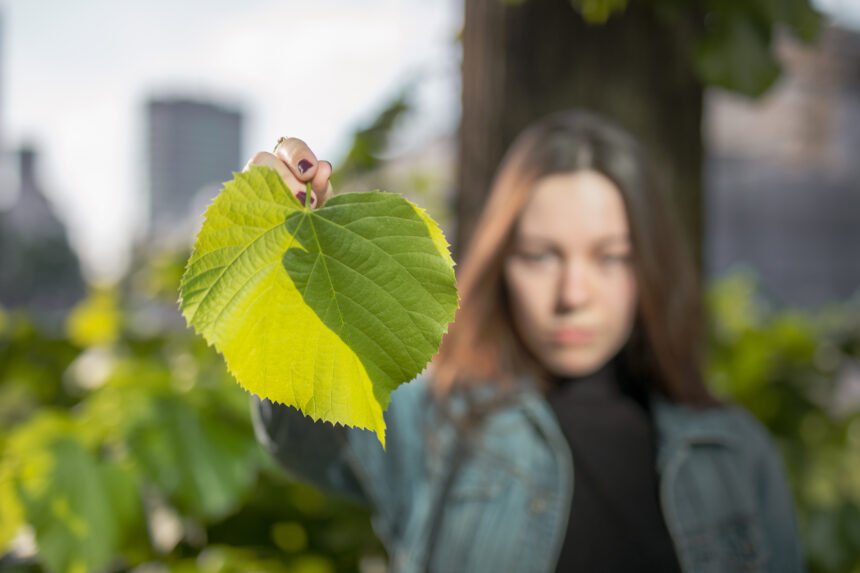 Mujer joven sosteniendo una gran hoja verde en un entorno urbano desenfocado.